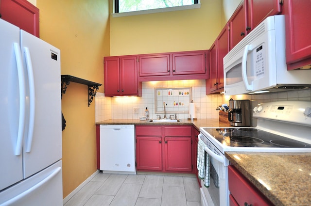 kitchen with white appliances, a sink, decorative backsplash, and red cabinetry