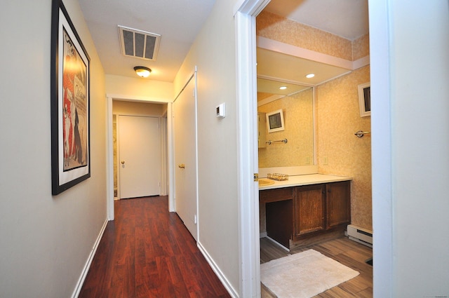 hall featuring dark wood-style flooring, baseboard heating, baseboards, and recessed lighting