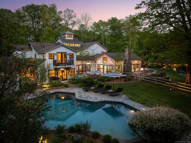 1580 Ponus Rdg, New Canaan, CT 06840 - back of house at dusk with a balcony, french doors, a patio area, an outdoor pool, and stucco siding