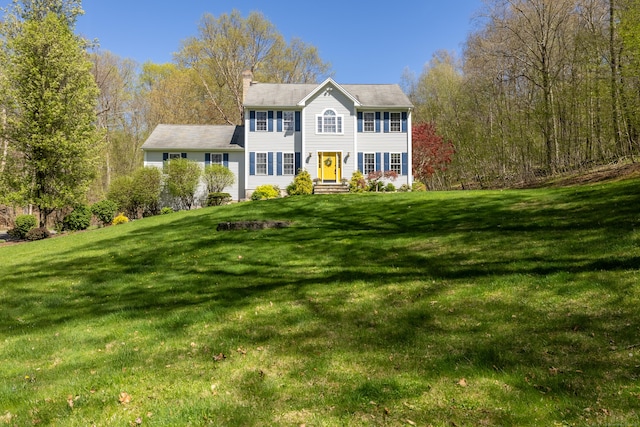colonial-style house featuring a chimney and a front yard