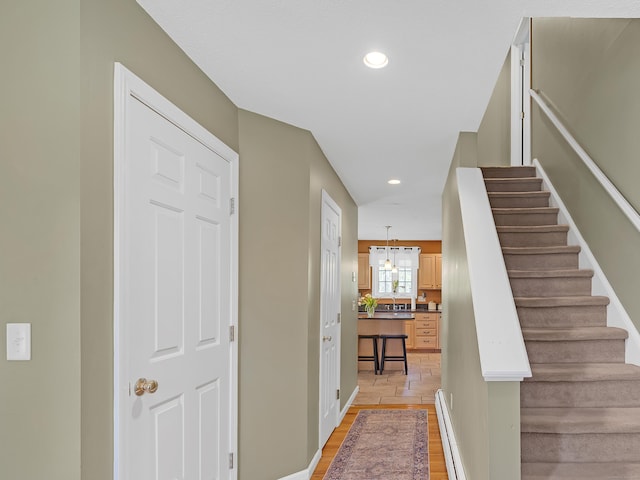 stairway with wood finished floors, recessed lighting, a baseboard heating unit, and a notable chandelier