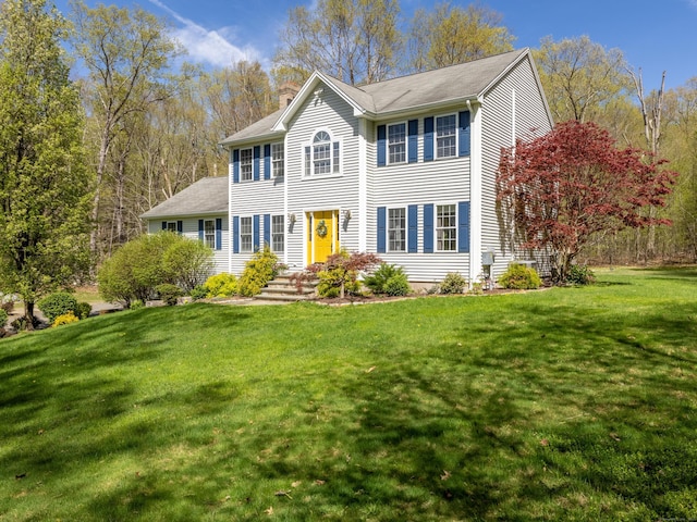 colonial home with a shingled roof, a chimney, and a front yard