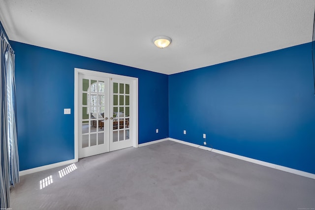 carpeted spare room featuring a textured ceiling, baseboards, and french doors