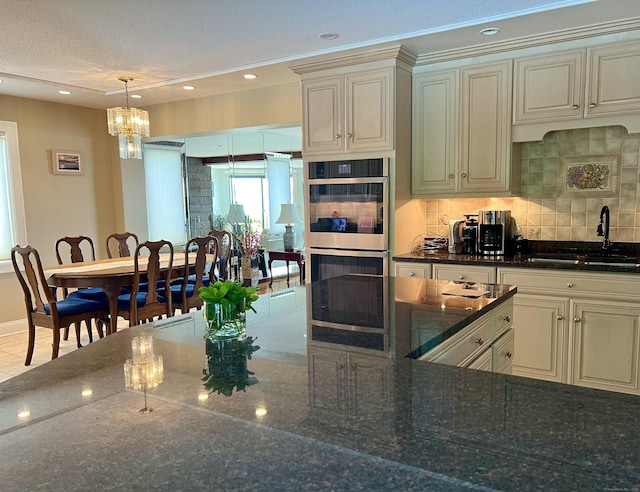 919 Pequot Ave, New London, CT 06320 - kitchen with double oven, backsplash, cream cabinets, dark stone countertops, and a chandelier