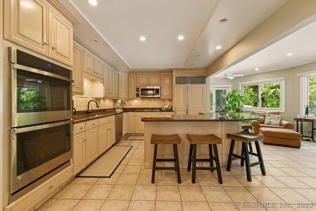 919 Pequot Ave, New London, CT 06320 - kitchen featuring stainless steel appliances, dark countertops, light tile patterned floors, open floor plan, and a breakfast bar