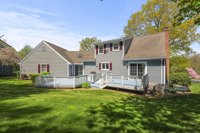 rear view of property with roof with shingles, a deck, a chimney, and a lawn
