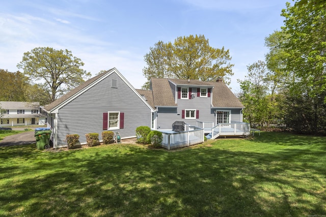 rear view of house with a wooden deck, a shingled roof, a chimney, and a lawn