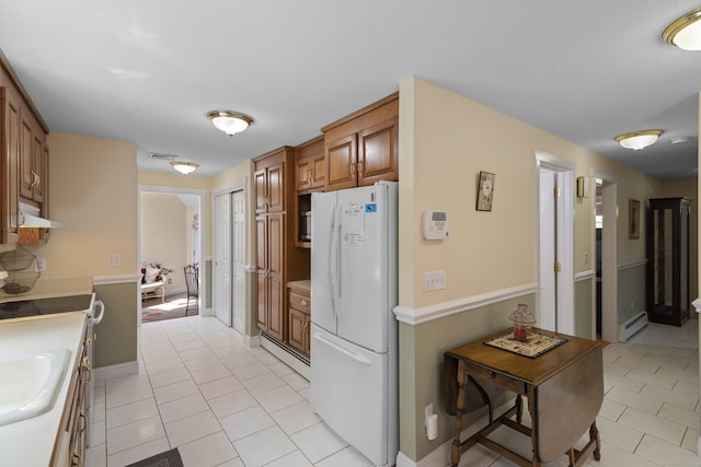 kitchen featuring brown cabinetry, a baseboard heating unit, freestanding refrigerator, under cabinet range hood, and light tile patterned floors