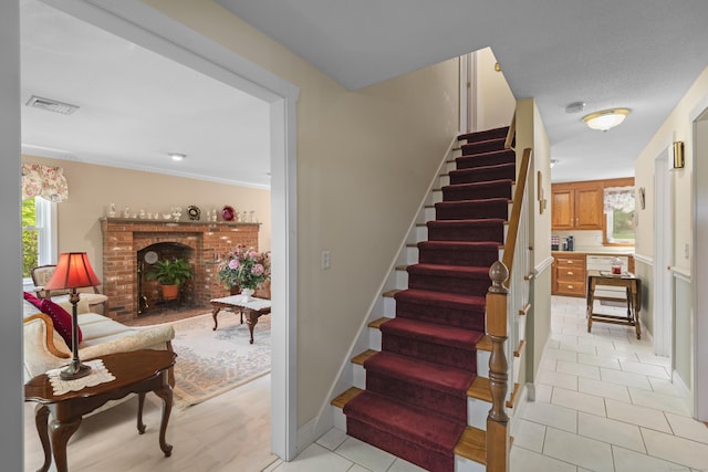 stairway with tile patterned flooring, visible vents, and a brick fireplace