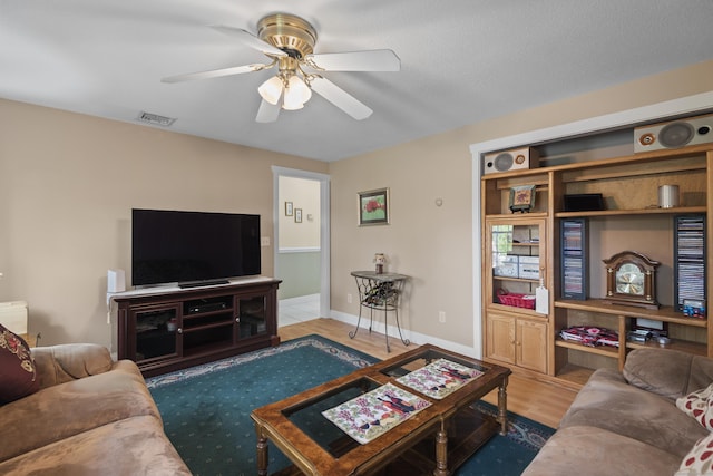 living area featuring baseboards, a ceiling fan, visible vents, and wood finished floors