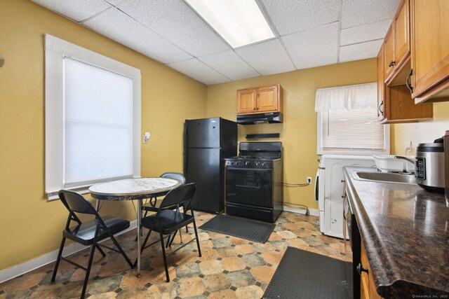 kitchen with black appliances, a sink, a drop ceiling, under cabinet range hood, and baseboards