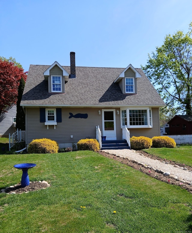 new england style home with roof with shingles, fence, a chimney, and a front yard