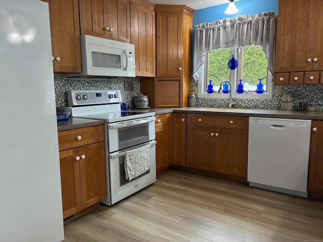 kitchen featuring a sink, brown cabinetry, white appliances, and decorative backsplash