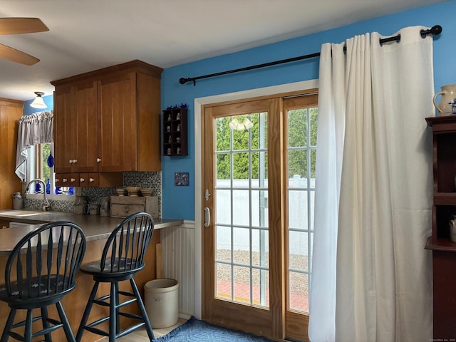 doorway to outside featuring a sink, ceiling fan, and wainscoting