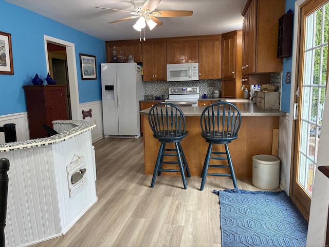 kitchen featuring white appliances, ceiling fan, a peninsula, decorative backsplash, and brown cabinets