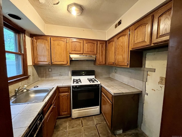 kitchen featuring a sink, tile counters, gas range, visible vents, and under cabinet range hood