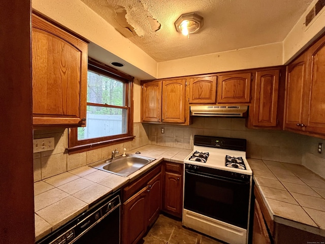 kitchen featuring tile countertops, under cabinet range hood, black dishwasher, gas stove, and a sink