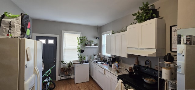 kitchen featuring black electric range, white fridge with ice dispenser, wood finished floors, a baseboard radiator, and under cabinet range hood