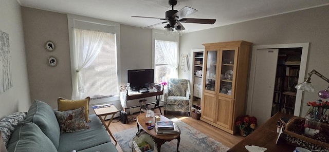 living area featuring light wood-style flooring, ceiling fan, and baseboard heating