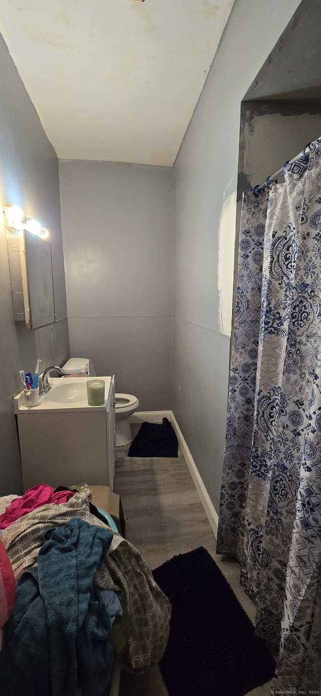 bathroom with a shower with curtain, wood finished floors, baseboards, vanity, and toilet