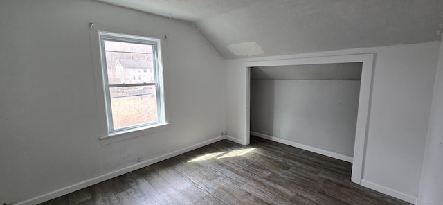 additional living space featuring dark wood-style flooring, baseboards, and vaulted ceiling