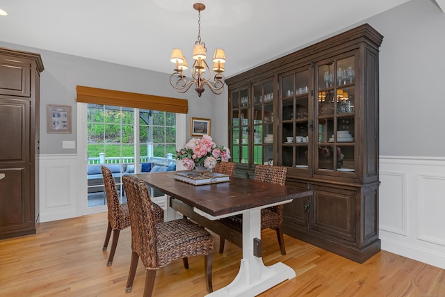 dining room featuring light wood-style floors, a notable chandelier, wainscoting, and a decorative wall
