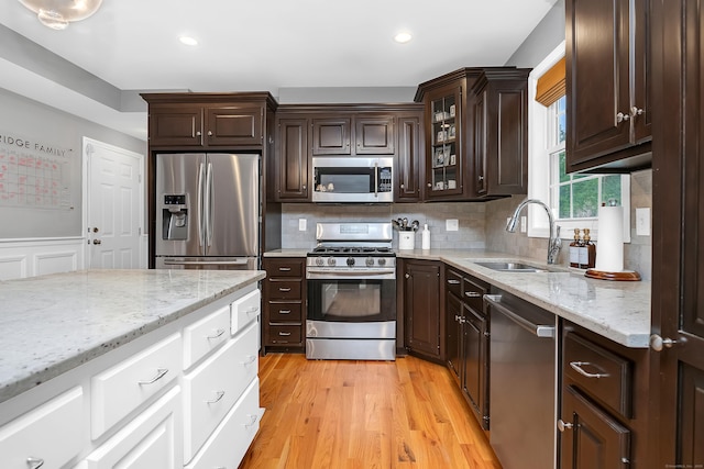 kitchen with dark brown cabinets, appliances with stainless steel finishes, a sink, light wood finished floors, and white cabinetry