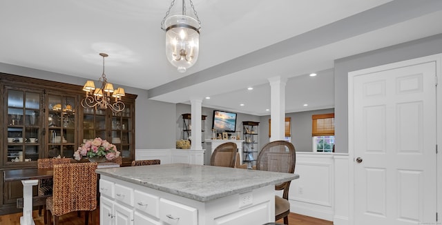 kitchen featuring light stone countertops, a decorative wall, a center island, decorative light fixtures, and ornate columns