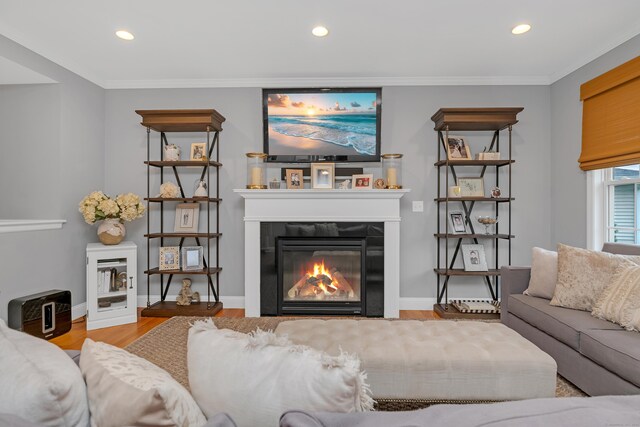 living room with recessed lighting, a glass covered fireplace, ornamental molding, and wood finished floors