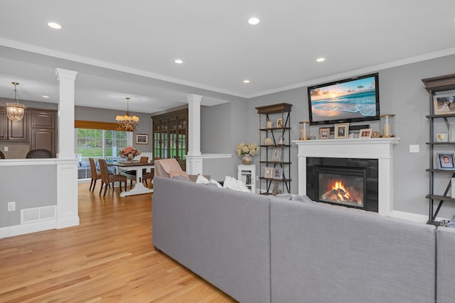 living area featuring an inviting chandelier, light wood finished floors, ornate columns, and visible vents