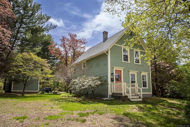 back of house with a lawn, roof with shingles, and a chimney