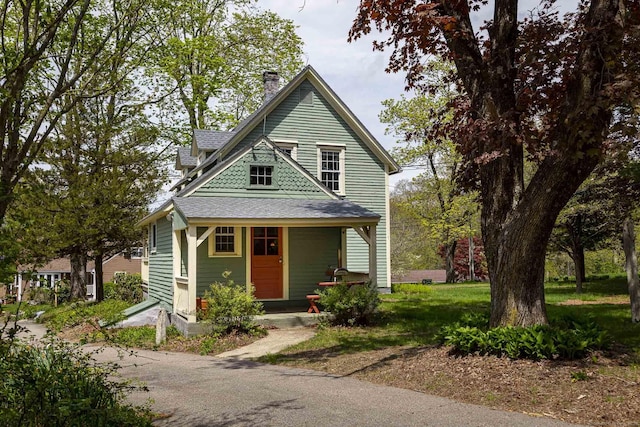 victorian home featuring a porch, a chimney, and roof with shingles