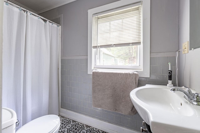full bath featuring tile walls, curtained shower, a sink, a wainscoted wall, and toilet