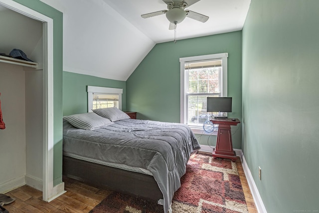 bedroom featuring baseboards, wood finished floors, vaulted ceiling, and multiple windows