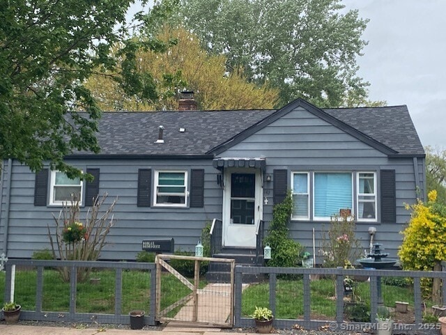 bungalow-style home with a shingled roof, a fenced front yard, a gate, and a chimney