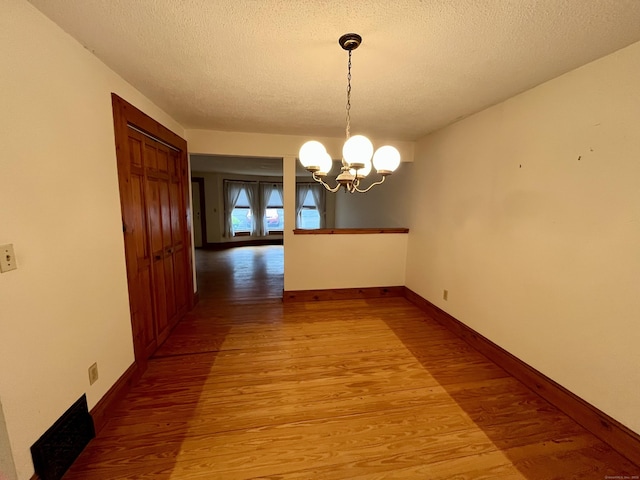 unfurnished dining area featuring baseboards, light wood finished floors, a chandelier, and a textured ceiling