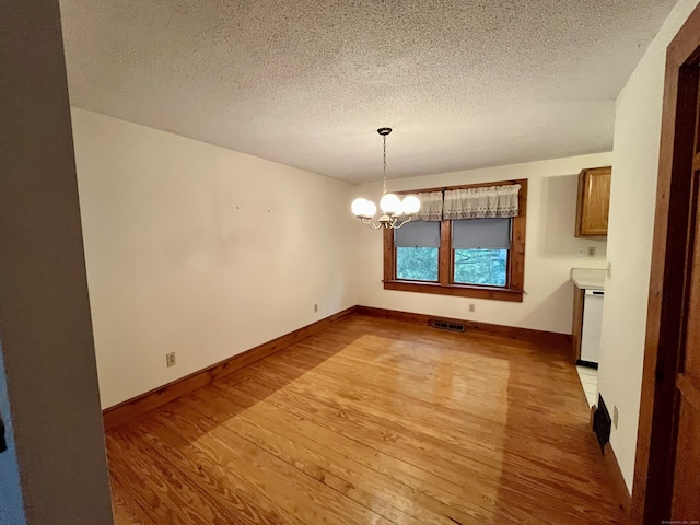 unfurnished dining area featuring a textured ceiling, visible vents, an inviting chandelier, baseboards, and light wood-style floors