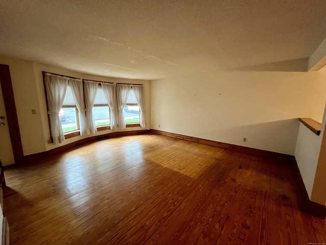 empty room featuring a textured ceiling, baseboards, and wood-type flooring