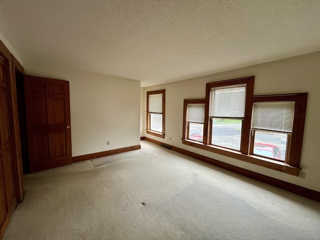 empty room with light carpet, a textured ceiling, baseboards, and visible vents