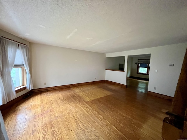 unfurnished living room featuring a textured ceiling, baseboards, and wood finished floors