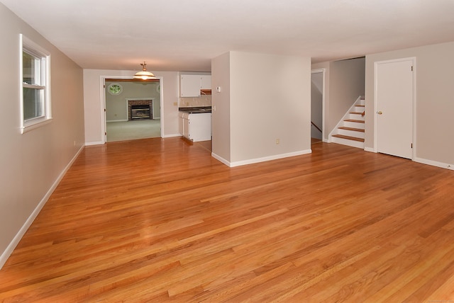 unfurnished living room with stairway, light wood finished floors, baseboards, and a brick fireplace