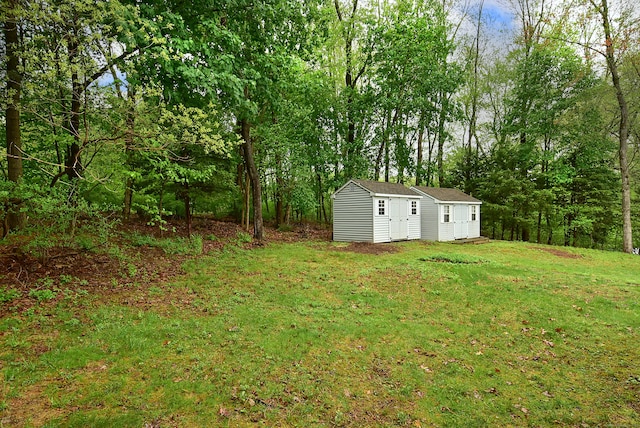 view of green lawn featuring an outdoor structure and a wooded view