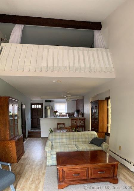 living room with a ceiling fan, baseboard heating, light wood finished floors, and a towering ceiling