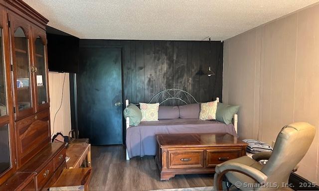 bedroom featuring a textured ceiling, a decorative wall, wood finished floors, and wooden walls