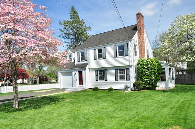 colonial house with a chimney, driveway, fence, a garage, and a front lawn