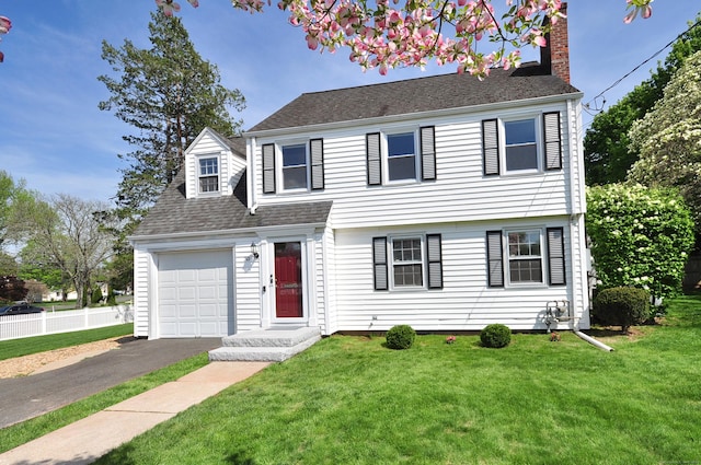 view of front facade with a chimney, driveway, a garage, roof with shingles, and a front lawn