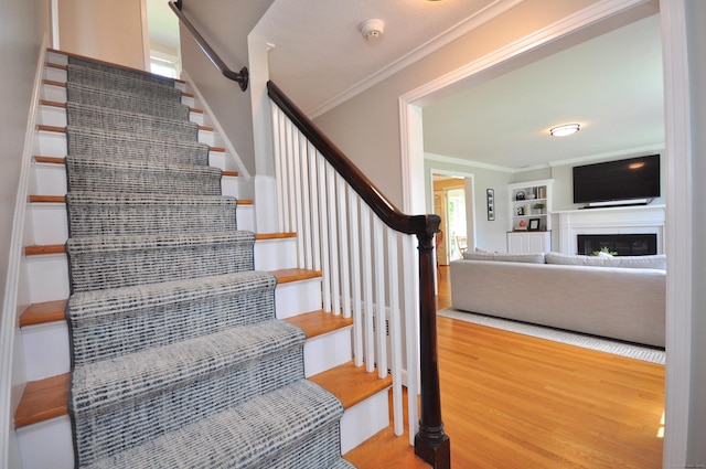 stairs with a fireplace, crown molding, and wood finished floors