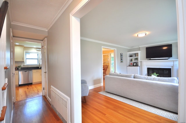living room with light wood-style floors, crown molding, a glass covered fireplace, and visible vents
