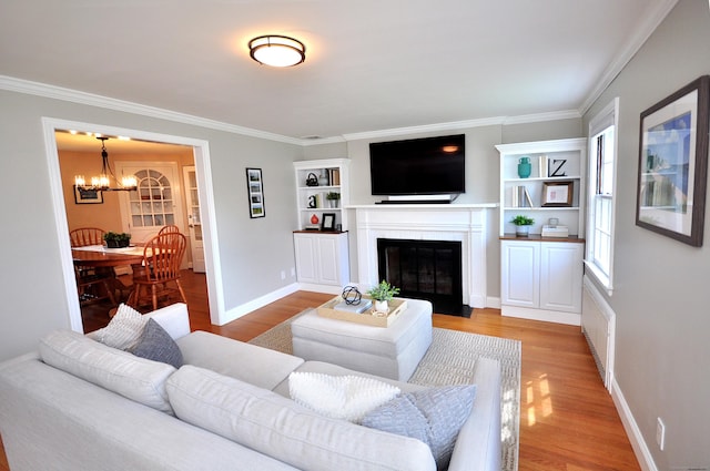 living room with ornamental molding, light wood finished floors, an inviting chandelier, and a fireplace with flush hearth