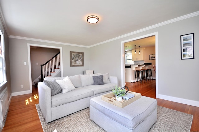 living area featuring stairway, light wood-style flooring, baseboards, and ornamental molding